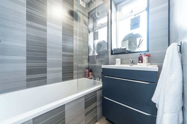 A modern bathroom with a glass-enclosed shower, a white bathtub, and a dark-colored vanity with a mirror above it.