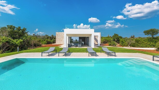 Un área de piscina moderna al aire libre con sillones de descanso y un cielo azul despejado.