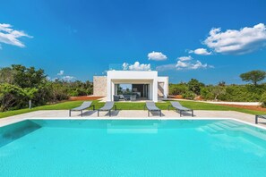 Un área de piscina moderna al aire libre con sillones de descanso y un cielo azul despejado.