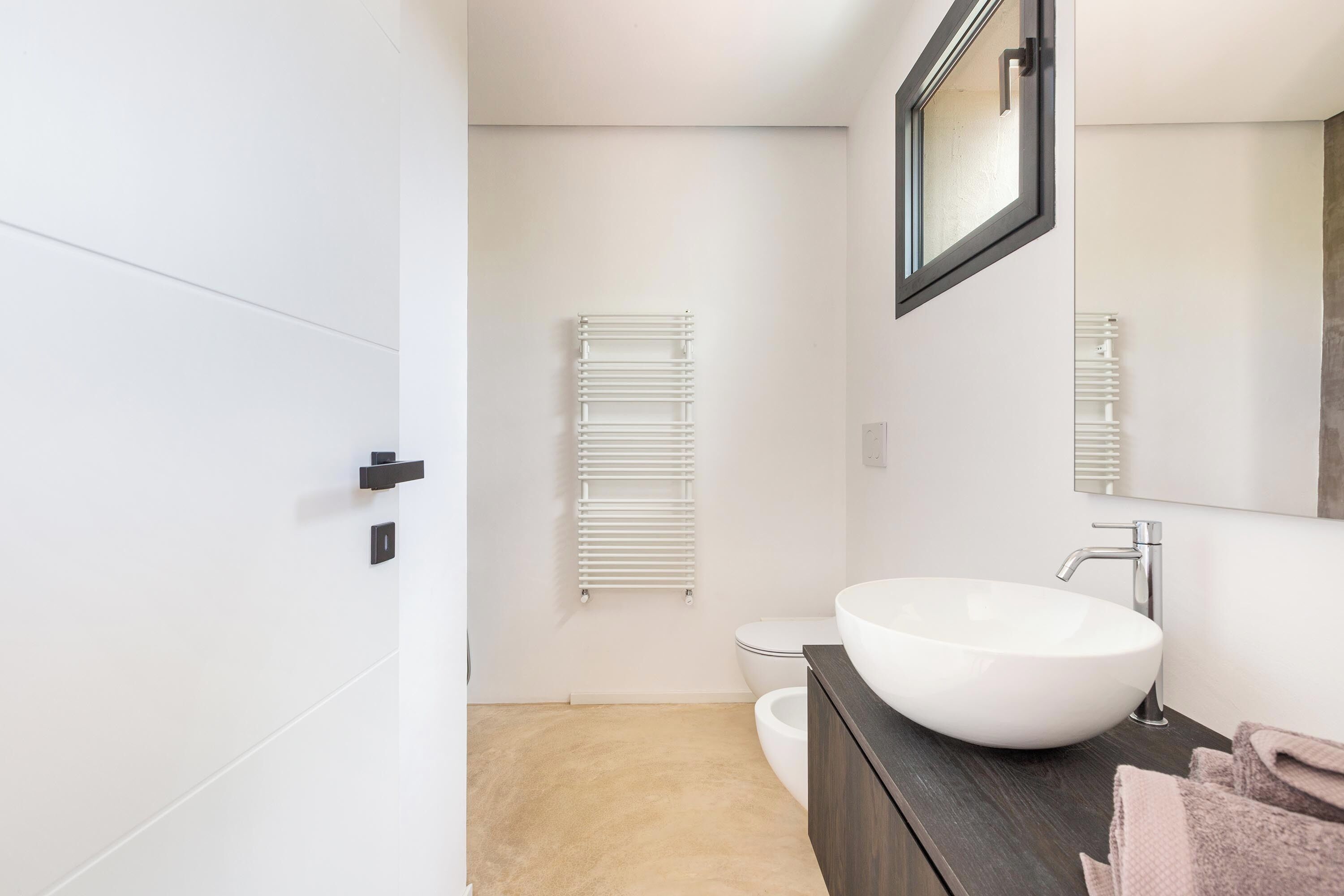 Un baño moderno con lavamanos blanco, tocador de madera oscura y un perchero para toallas.