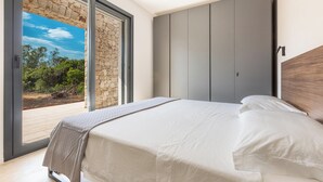 Un dormitorio con una cama grande, una pared de piedra y una puerta corrediza que da a un espacio exterior.