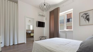 A bedroom with a bed, a television, a window with curtains, and a wall-mounted air conditioner.