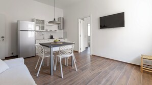 A modern kitchen with white cabinetry, a dining area with a table and chairs, and a flat-screen TV mounted on the wall.