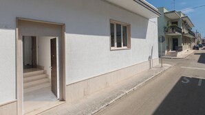 A residential building with a clean facade, a visible entrance with steps, and a small window.