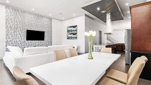 Ein modernes Wohnzimmer mit einem weißen Sofa, einem Esstisch und einer Küche im Hintergrund.