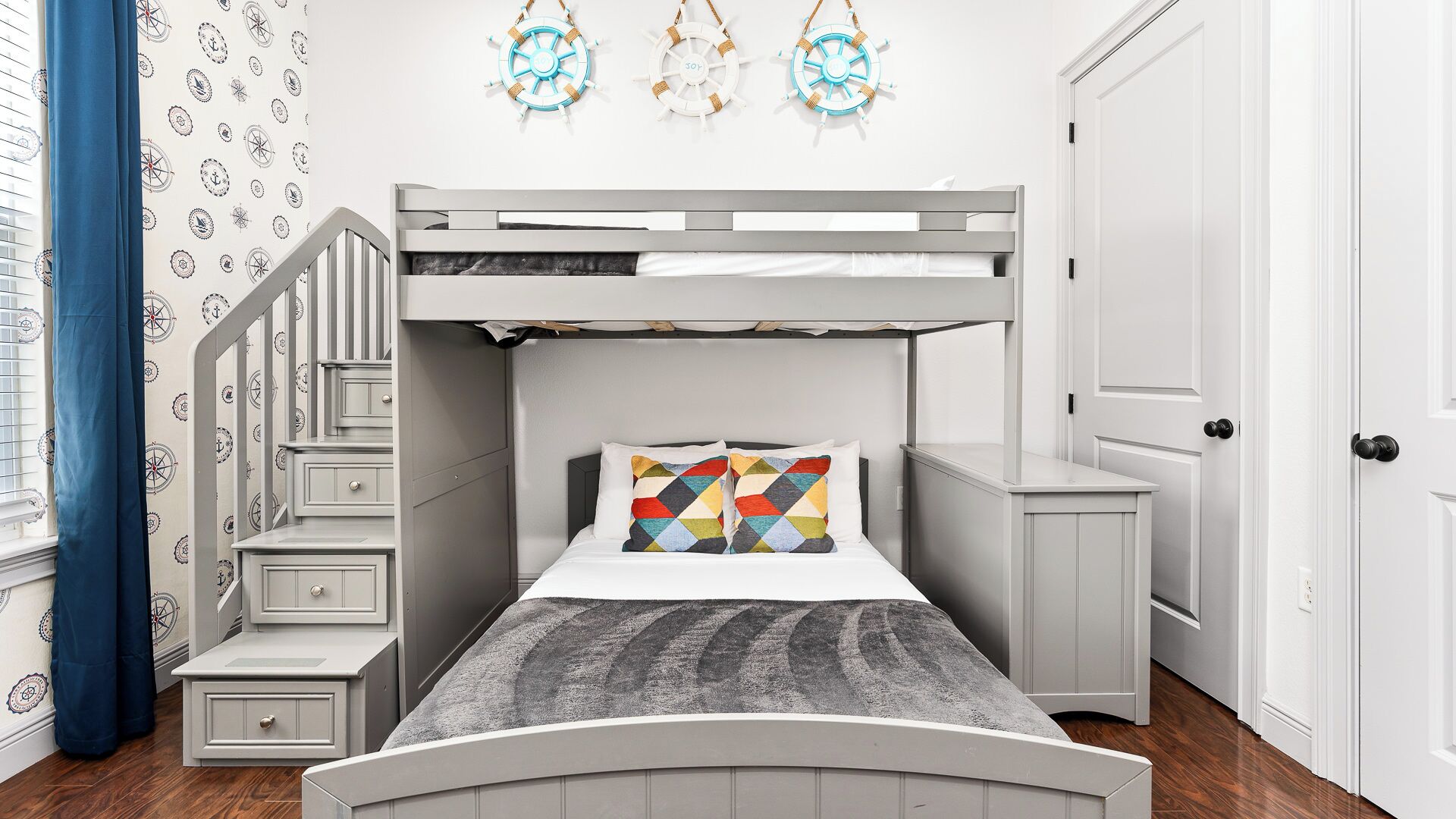 A bunk bed room with a desk and drawers, nautical wall decor, and a door.