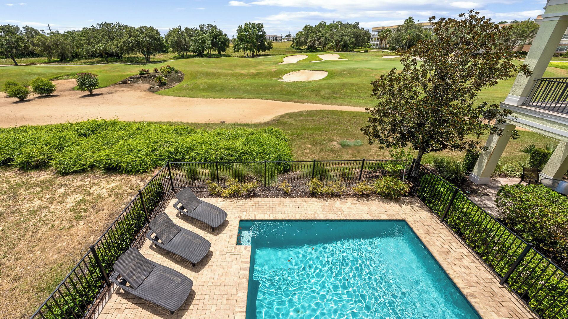 A swimming pool with lounge chairs, surrounded by a brick patio and a view of a golf course.