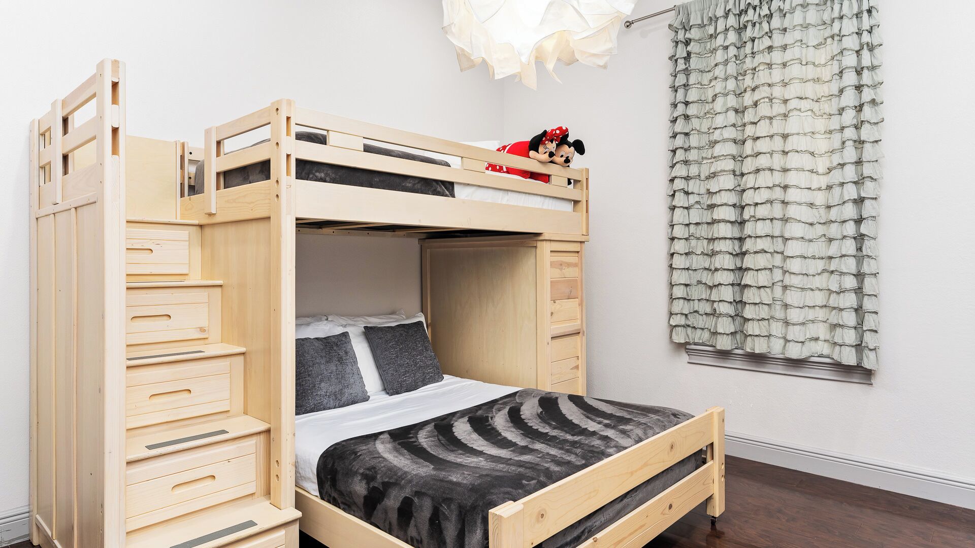 A bunk bed with a lower bed and a loft bed, both made of wood. There is a small Mickey Mouse plush toy on the loft bed.
