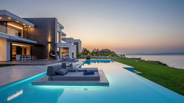 Una casa moderna con piscina, mobiliario exterior y vista al mar.