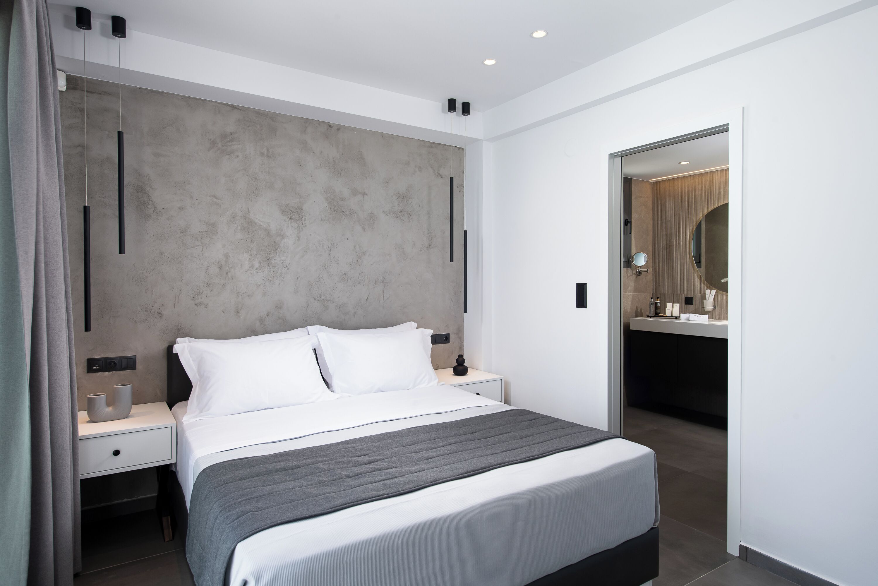 A modern bedroom with a large bed, bedside tables, a wardrobe, and a bathroom visible through an open door.
