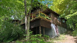 Una cabaña rústica con balcón de madera, rodeada de un bosque denso.