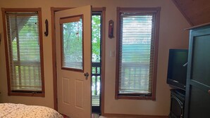 Un dormitorio con una cama, un televisor y tres ventanas con persianas.
