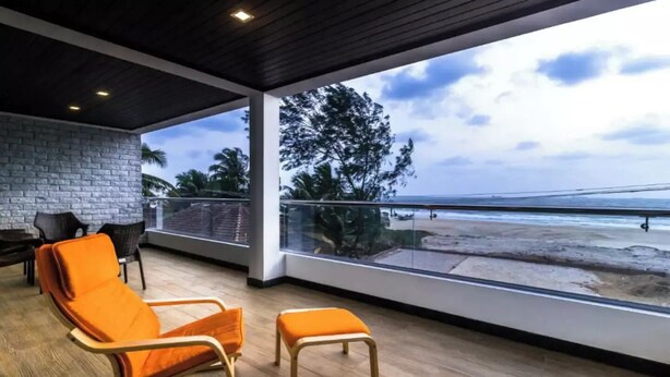 A balcony with wooden flooring, orange chairs, and a view of the beach. - Raj Sea Front Beach Resort 102 (Mangaluru)