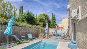 Piscina con sillas de descanso y sombrillas, rodeada por una terraza de madera y un muro de piedra.