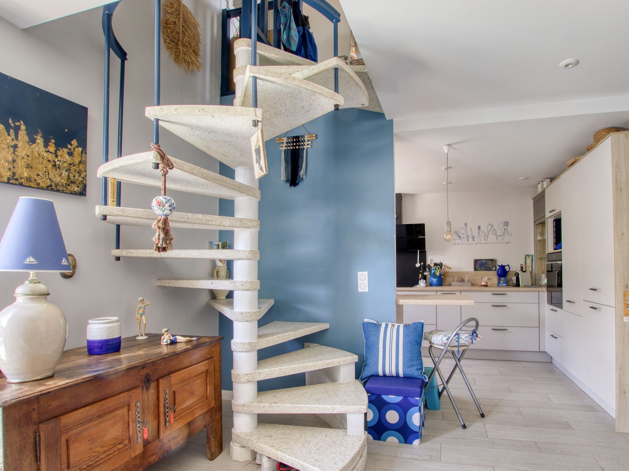 Eine spiralförmige Treppe in einer modernen Küche mit blauer Akzentwand, Holzschränken und einem Essbereich mit Stuhl und Tisch.