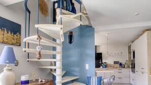 Una escalera de caracol en una cocina moderna con una pared azul decorativa, armarios de madera y un comedor con una silla y una mesa.