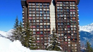 Un hôtel de grande hauteur doté de nombreux balcons, entouré de montagnes enneigées et d’arbres à feuilles persistantes.