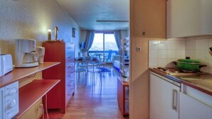 Une petite cuisine équipée d’une machine à café, d’un meuble rouge et d’une casserole verte sur la cuisinière.