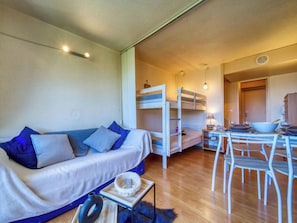 Un espacio habitable compacto con sofá, literas, una mesa de comedor con sillas y una pequeña cocina.