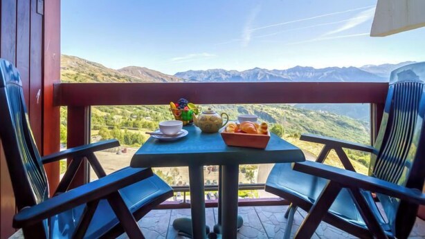 Un balcon avec une table dressée pour deux personnes, offrant une vue sur un paysage montagneux.