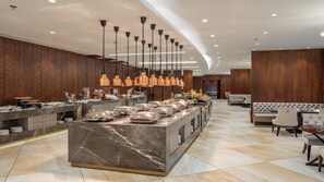 A modern buffet area with marble countertops, copper pendant lights, and a variety of food options. - Wirgan Al Noor, Tapestry Collection by Hilton (Makkah)