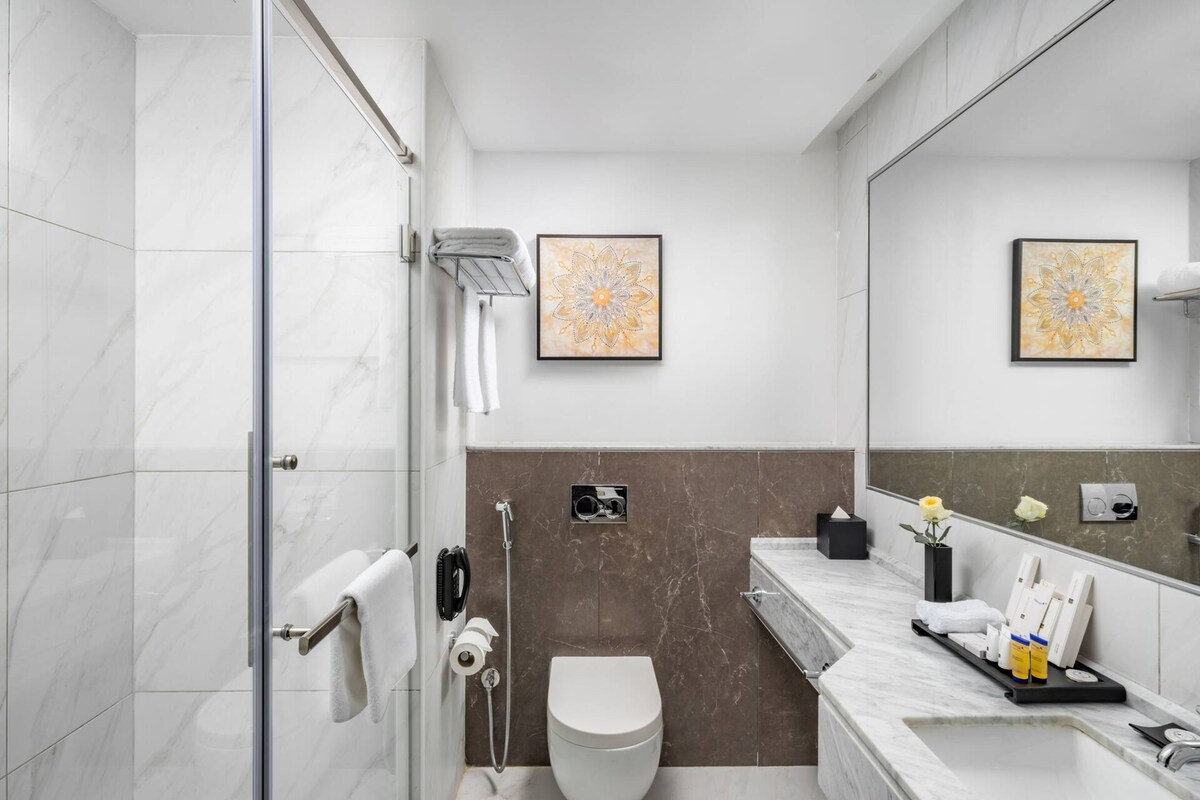 A modern bathroom with a glass shower enclosure, a toilet, and a marble vanity with a sink and towel rack.