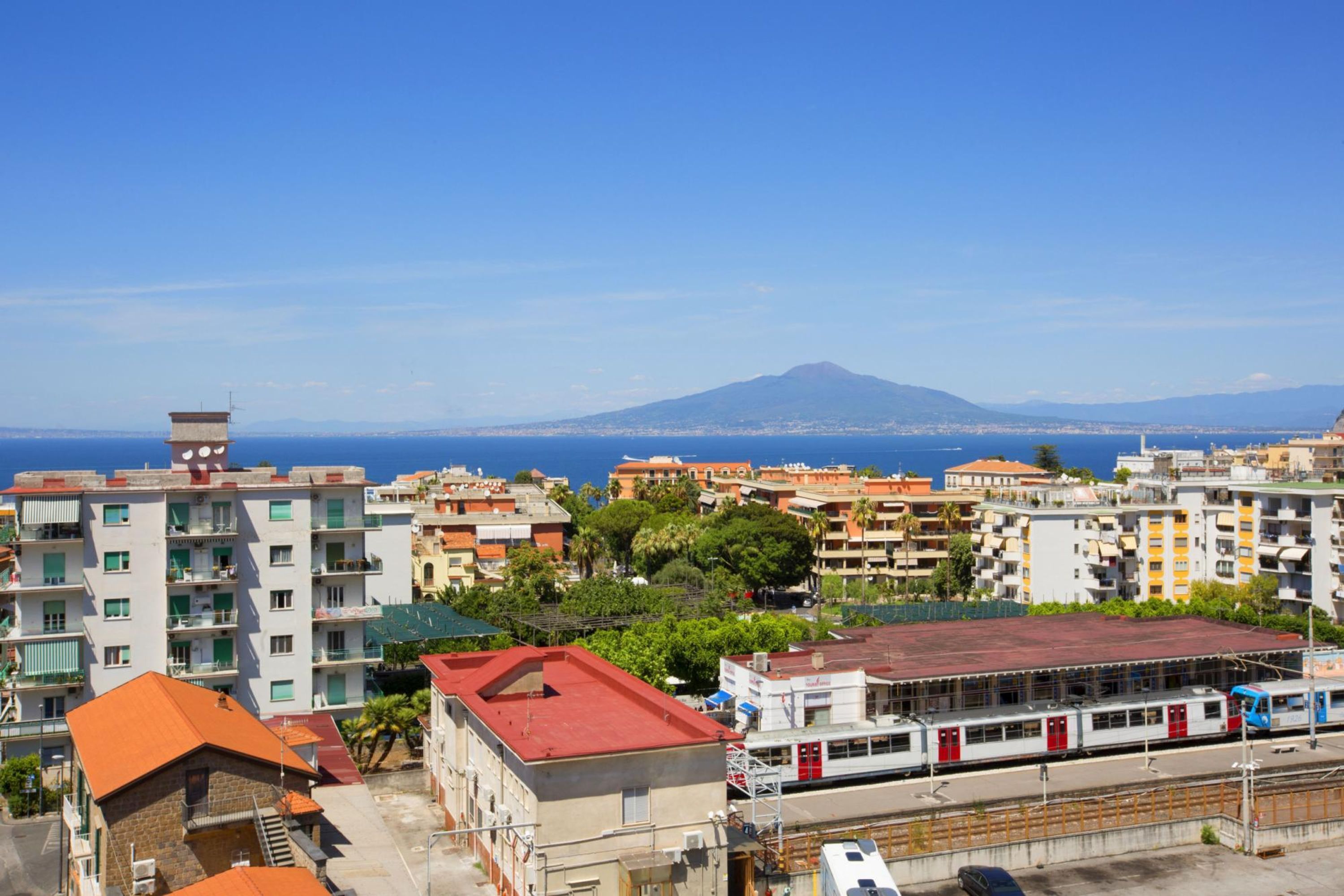 Paesaggio urbano con una stazione ferroviaria, edifici e una montagna sullo sfondo.