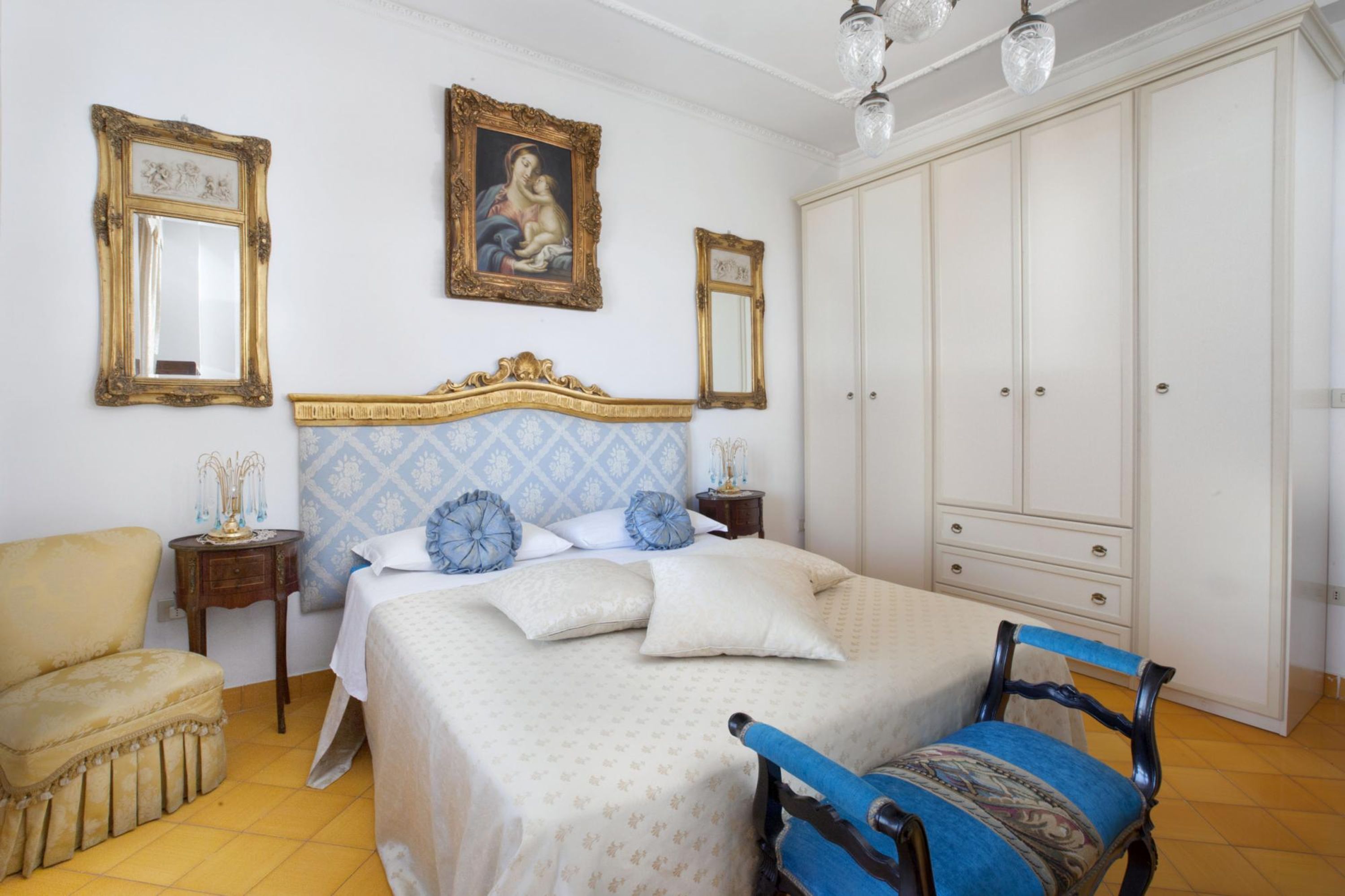A bedroom with a bed, a chair, a wardrobe, and two mirrors.