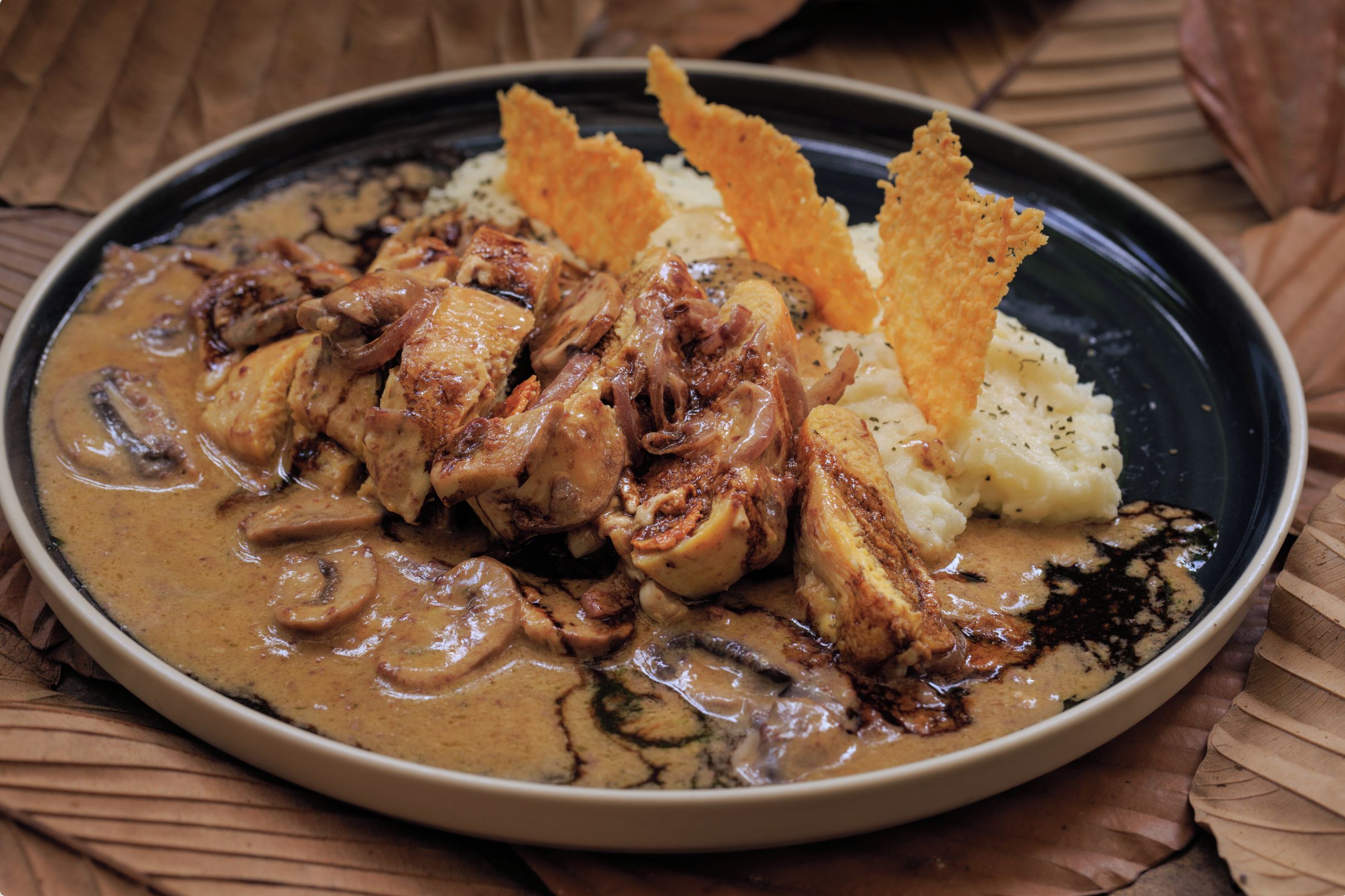 A plate of food with a creamy sauce, meat, mushrooms, and potato side.