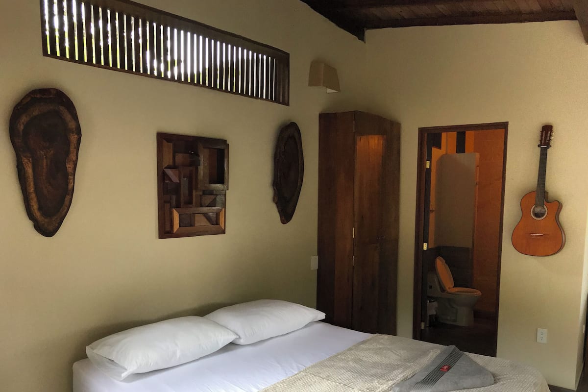A bed with white linens, a wooden headboard, and a decorative wall piece above it.