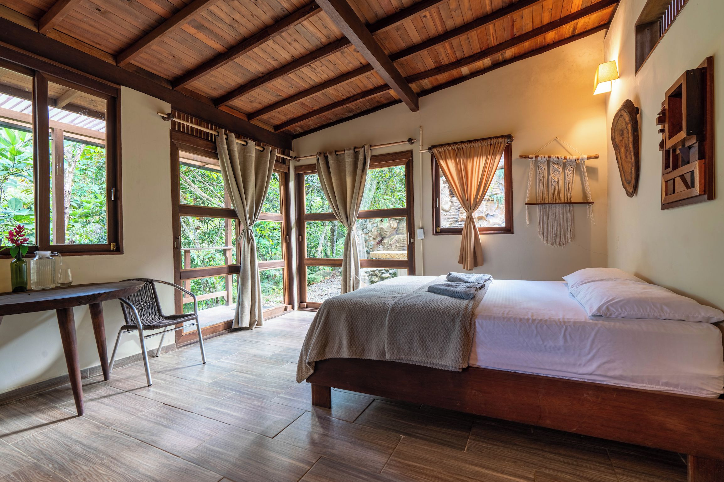 A room with a bed, a desk, and large windows.