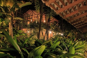 A multi-level wooden structure surrounded by dense tropical foliage at night. - Ritmo Del Rio - Hotel y Restaurante (San Rafael)