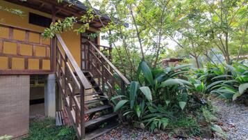 A wooden staircase leading to a yellow building with a covered porch, surrounded by lush greenery and tropical plants.