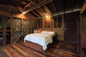 Quarto de madeira com cama, parede de pedra e vigas no teto.
