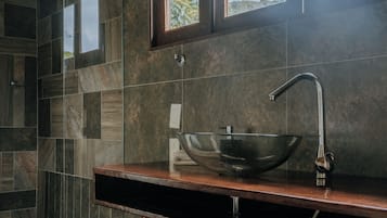 A modern bathroom with a large vessel sink, a wooden vanity, and a window with a view of greenery.