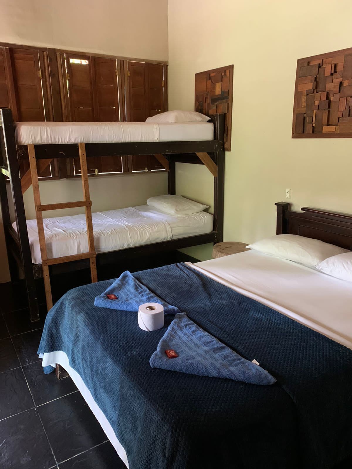 A bunk bed room with a blue blanket and pillows, a wooden headboard, and a wall-mounted artwork.
