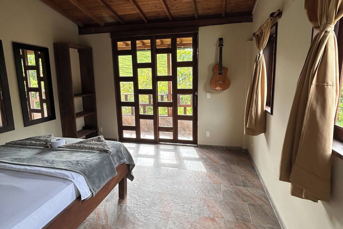 A bedroom with a bed, a guitar, and a view through a door.
