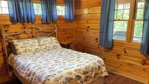 A wooden cabin room with a bed, curtains, and a window. - Cozy mountain cabin 15 minutes from historic downtown, 3 miles from ORV PARK  (Hot Springs National Park)