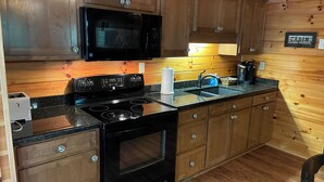 A kitchen with wooden cabinets, a black stove, a microwave, and a sink. - Cozy mountain cabin 15 minutes from historic downtown, 3 miles from ORV PARK  (Hot Springs National Park)