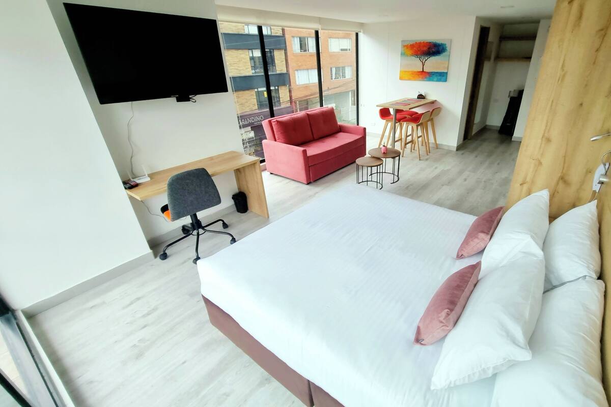 Une chambre d’hôtel moderne avec un grand lit, un bureau avec une chaise, un canapé rouge et un coin repas avec deux chaises.