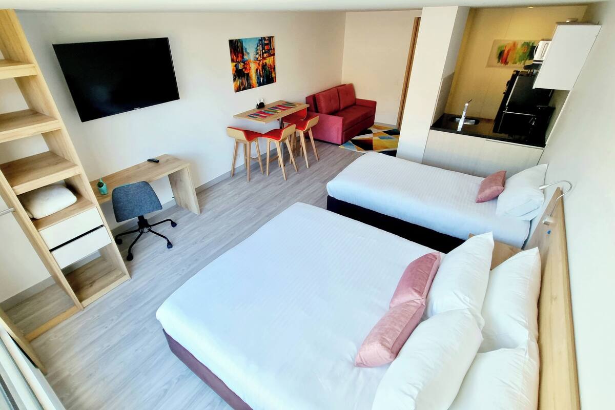 Une chambre d’hôtel avec deux lits, un bureau avec des chaises, une télévision et une kitchenette.