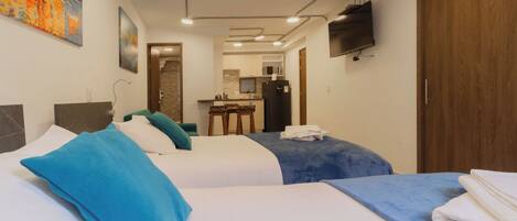 A hotel room with two beds, a kitchenette, a TV, and artwork on the walls.