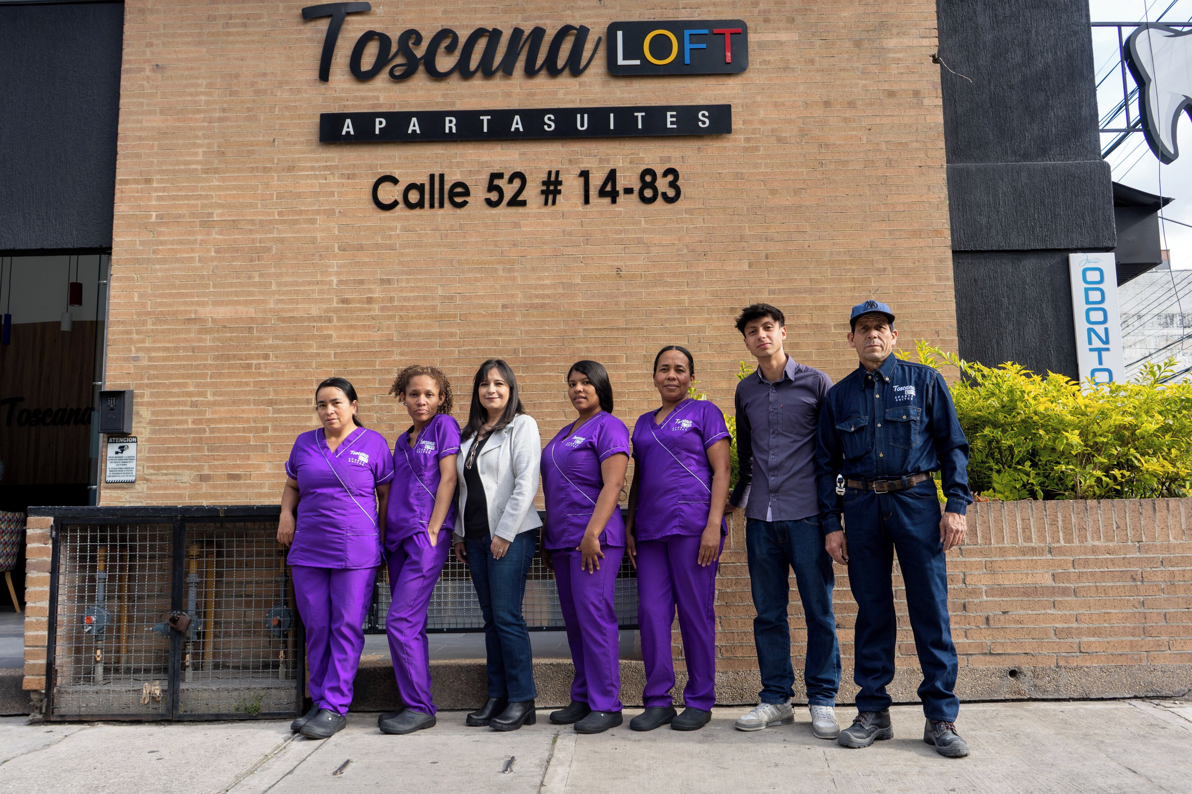 A group of people standing in front of a building with a sign that reads "Toscana LOFT APARTS SUITES Calle 52 # 14-83."