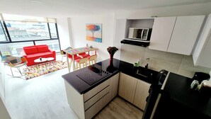 A modern kitchen with a black countertop, white cabinets, and a microwave. There is a red sofa and a colorful rug in the living area.