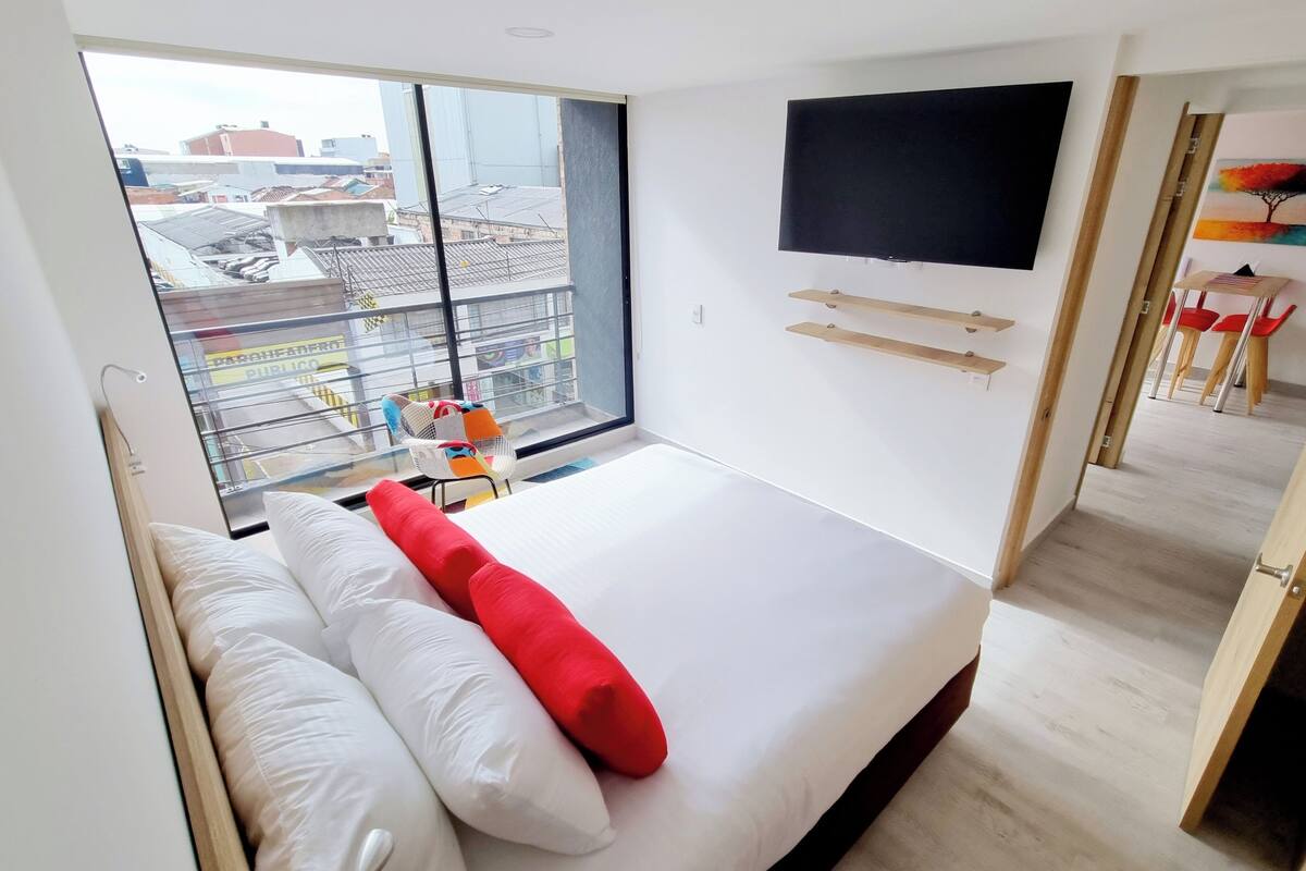 Une chambre d’hôtel moderne dotée d’un grand lit, d’un téléviseur fixé au mur et offrant une vue sur la ville grâce à une grande fenêtre.