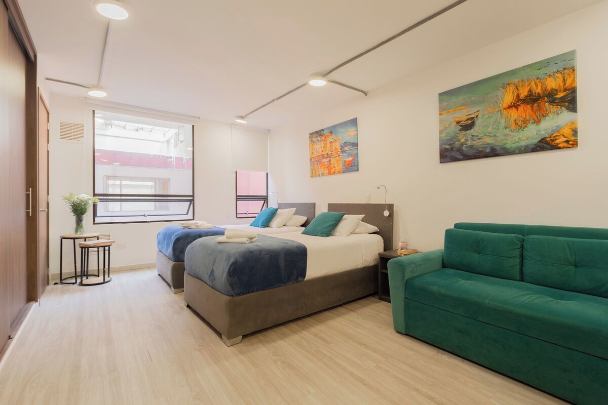 A modern hotel room with a bed, a green sofa, and two paintings on the wall.