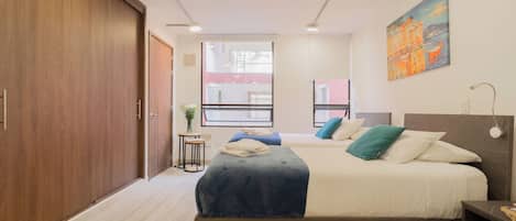 A modern bedroom with a large bed, a wardrobe, a small table with a plant, and a painting on the wall.