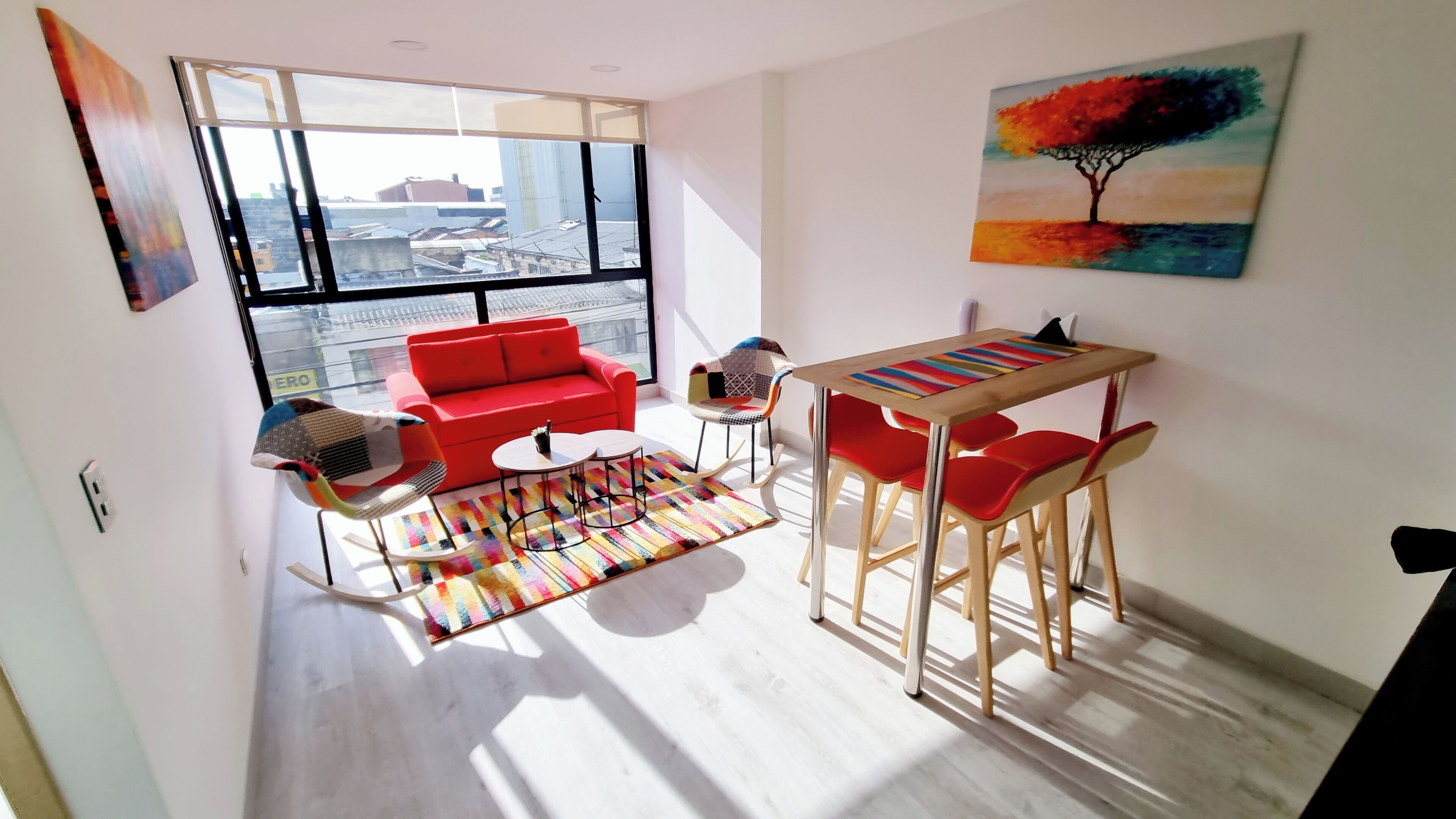 A modern living room with a red sofa, a colorful rug, and a dining area with red chairs and a wooden table.