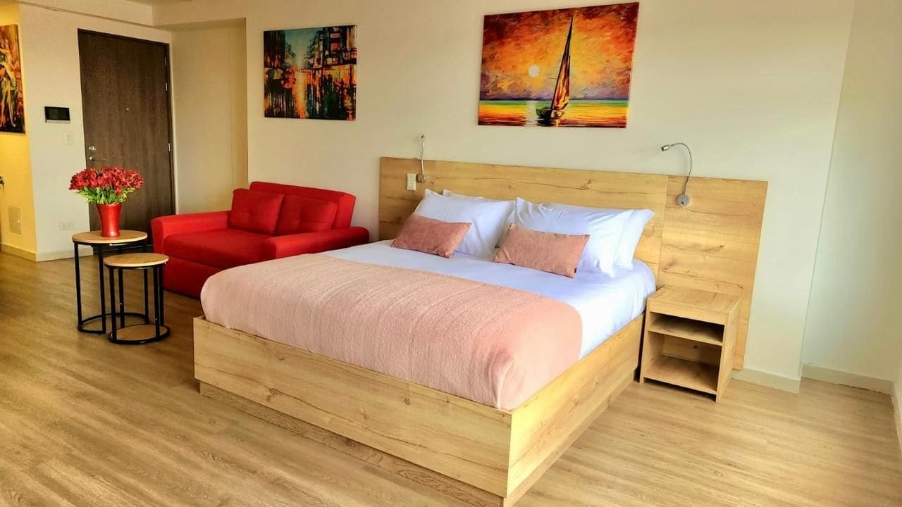 Een hotelkamer met een houten bed, een rode bank, een klein tafeltje met een bloevas en kunstwerken aan de muur.