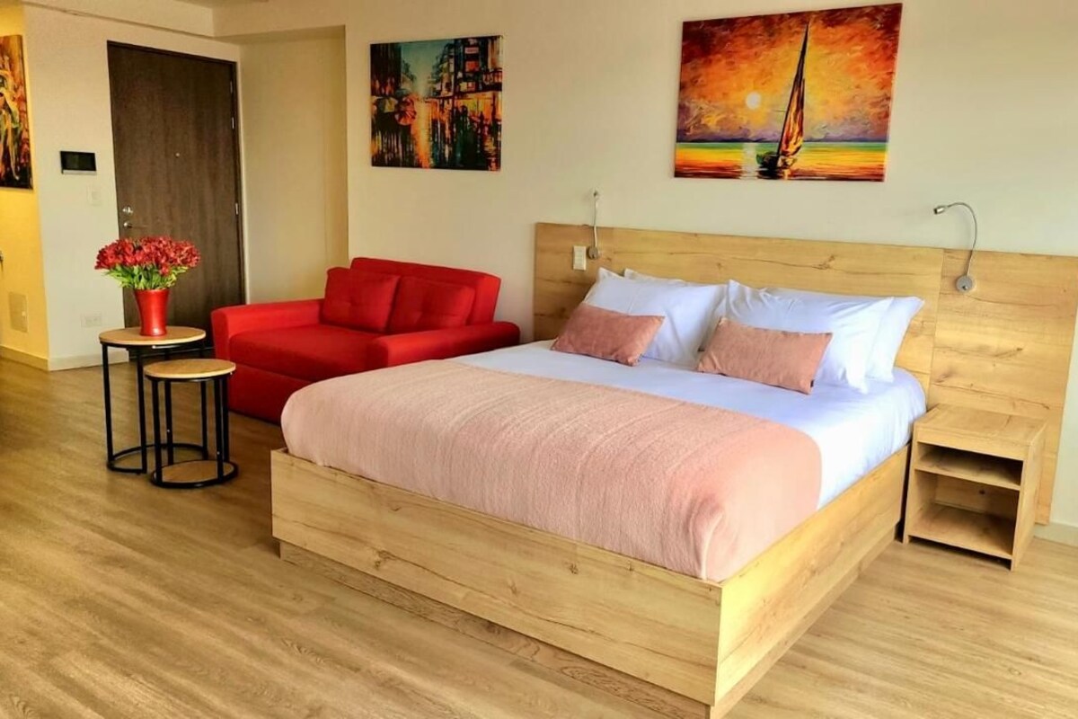 A hotel room with a wooden bed, a red sofa, a small table with a vase of flowers, and artwork on the walls.